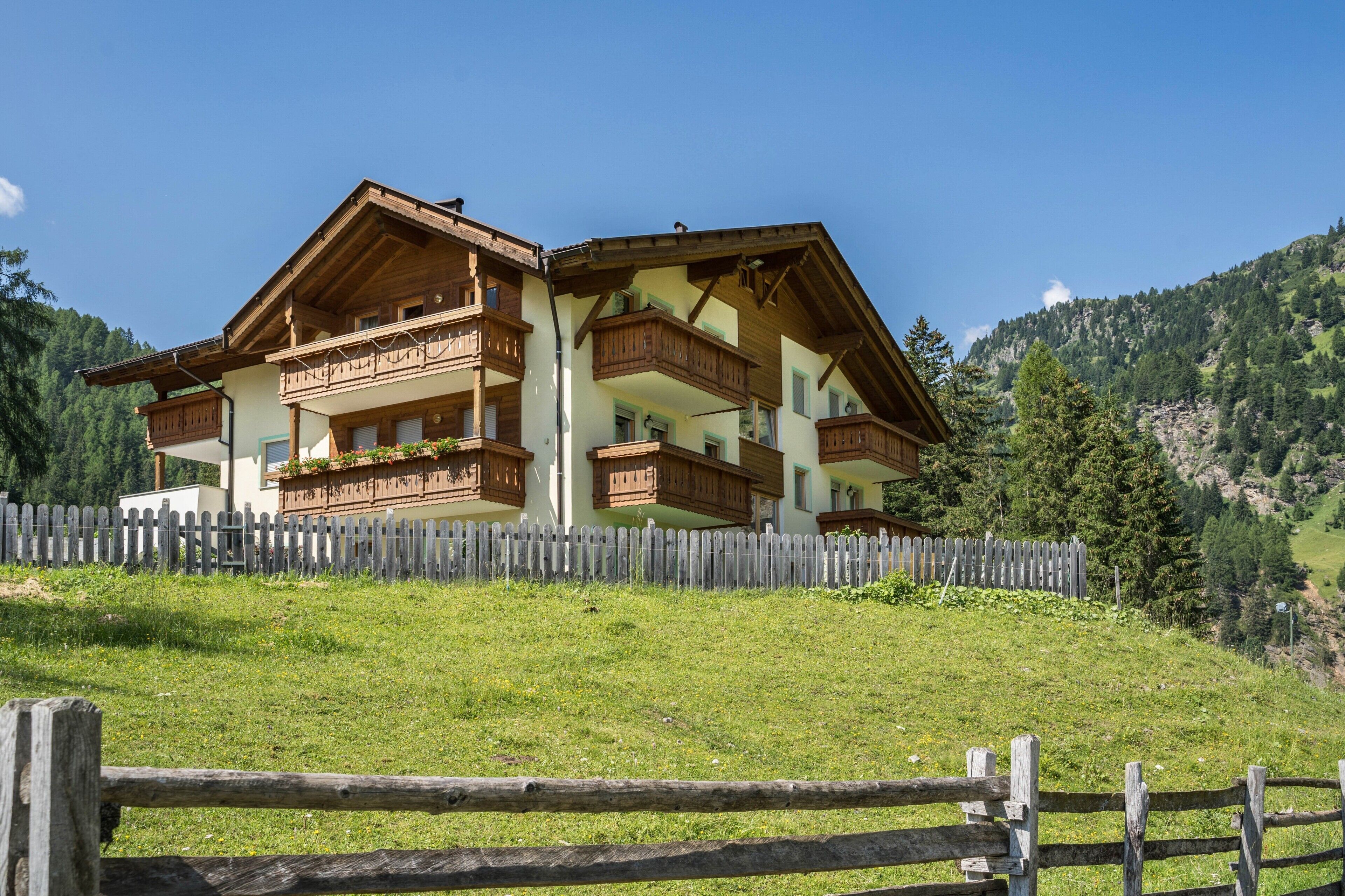 Un chalet en bois à deux étages, doté de balcons et entouré d’une clôture en bois, situé dans une région montagneuse.