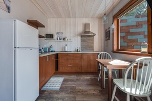 Een keuken met houten kastjes, een witte koelkast, een magnetron en een raam met uitzicht.