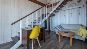 Una scala con ringhiere in legno, un'area da pranzo con una sedia gialla, un tavolo rotondo in legno e un divano grigio con una coperta gialla.