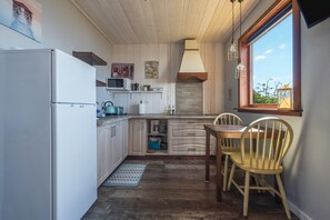 Een keuken met houten kastjes, een koelkast, een magnetron en een eettafel met stoelen.