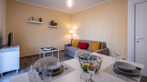 Una sala moderna con un sofá, una mesa de comedor para dos personas y un televisor sobre un mueble.