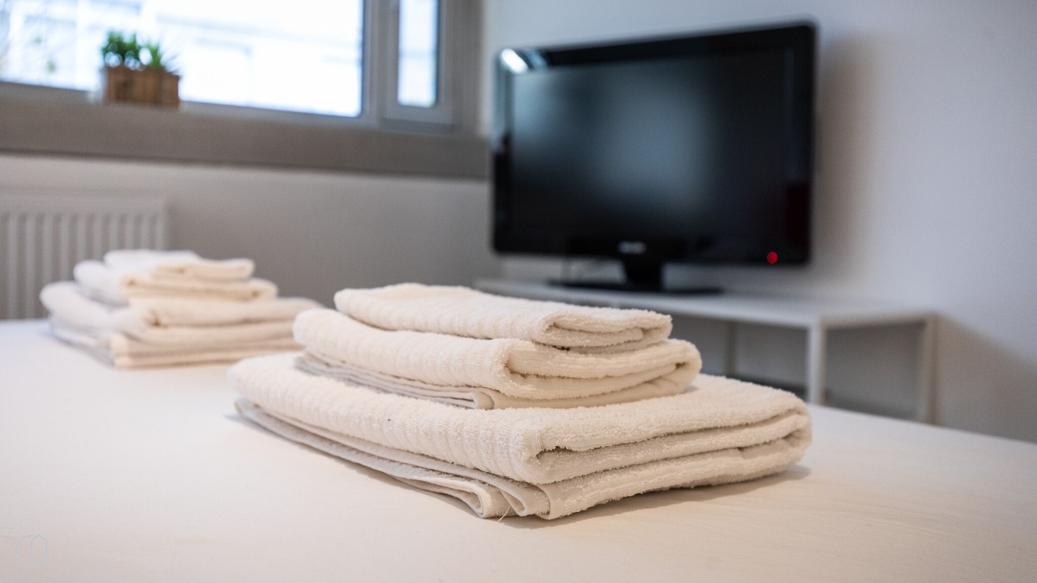 A neatly arranged stack of towels on a table in a room with a television on a stand.