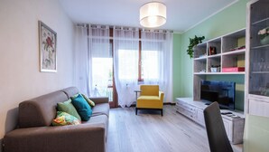Ein Wohnzimmer mit einer Couch, einem gelben Sessel, einem Fernseher und einem Bücherregal.