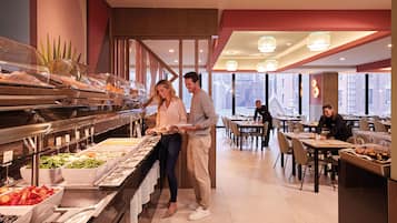A buffet area with various food options, a seating area with tables and chairs, and a view of the city through large windows.