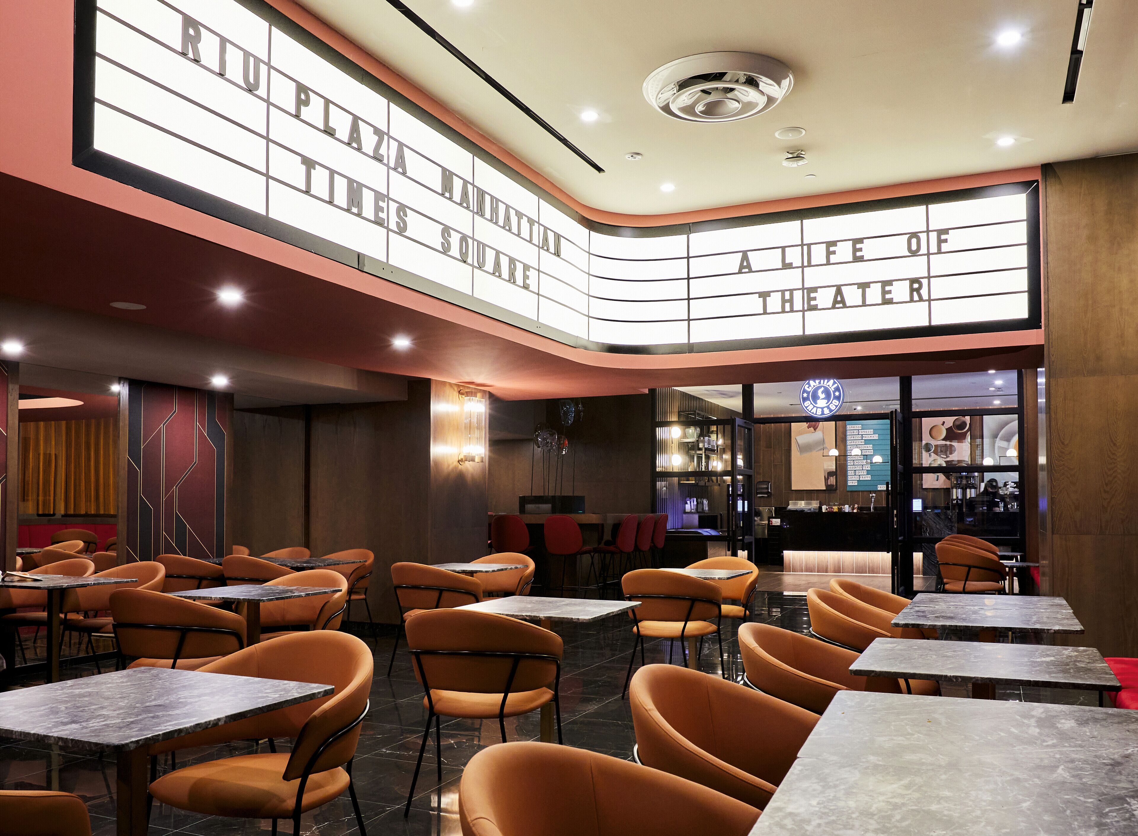 A restaurant with multiple dining tables and orange chairs, a bar area, and a large illuminated sign above the seating area.