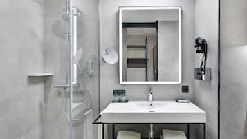 Un baño moderno con ducha de vidrio, lavamanos blanco y encimera negra, y un espejo grande.
