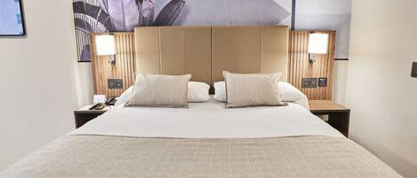 Une chambre d’hôtel avec un grand lit, deux tables de chevet, une tête de lit et une œuvre d’art accrochée au mur.