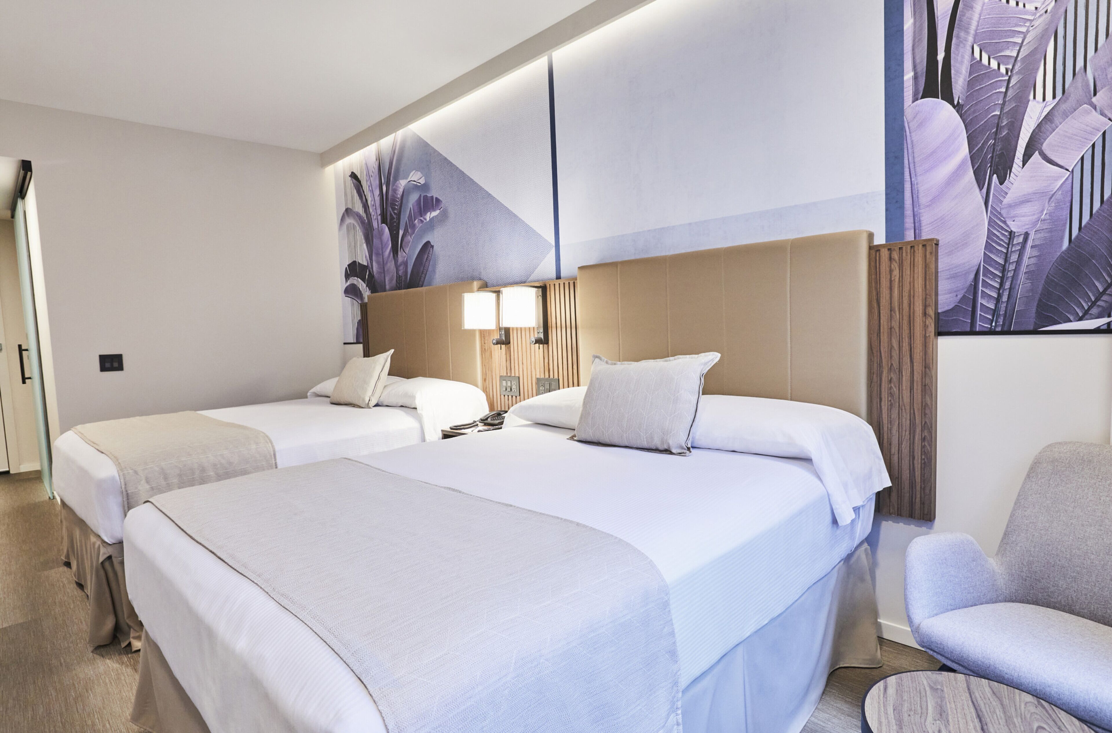 Quarto de hotel com duas camas, um espaço de estar e um grande mural na parede.