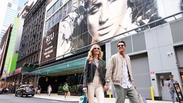 A building with a Times Square Hotel sign, a large billboard, and a pedestrian walkway.