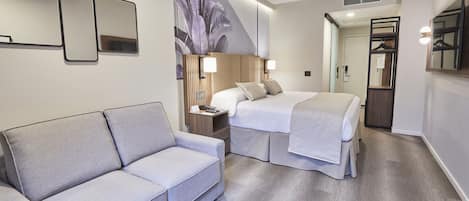 A modern hotel room with a sofa, a bed, a nightstand, and a large mirror.