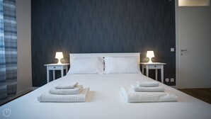 A neatly made bed with two pillows, two bedside tables with lamps, and two folded towels on the bed.