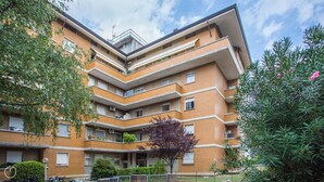 A multi-story residential building with a brick facade, multiple balconies, and a central courtyard with a tree.