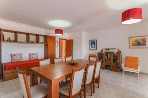 A dining area with a wooden table, chairs, a red pendant light, and a sofa with cushions.