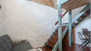 Un escalier avec des marches en bois et une rampe bleu clair, menant à une pièce dont un mur est recouvert d’un revêtement texturé blanc et qui contient un canapé gris.