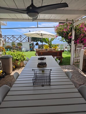 Een overdekt terras met een tafel, stoelen, een plafondventilator en potplanten.