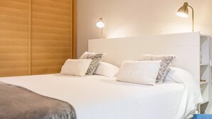 Una cama bien hecha con sábanas blancas y almohadas estampadas, un cabecero de madera y dos lámparas de noche.
