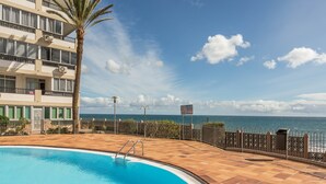 Una piscina con una palmera, vista al océano y un edificio con balcones.