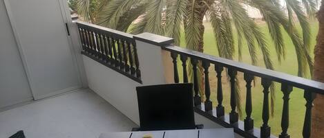 Un balcón con mesa y sillas, una planta en maceta y vistas a palmeras.