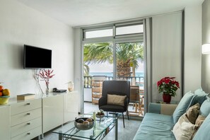 Un salon équipé d’un téléviseur, d’une table basse en verre, d’un canapé, d’un fauteuil et offrant une vue sur la mer grâce à de grandes fenêtres.