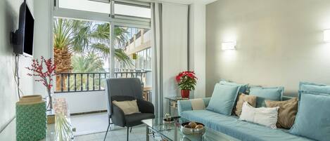 Una sala de estar moderna con una mesa de centro de vidrio, un sofá, una silla y un televisor montado en la pared.