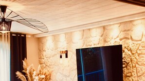 Un salon moderne avec un mur en pierre, un téléviseur à écran plat, une table basse en bois, un canapé et un coin repas avec des chaises et une petite table.