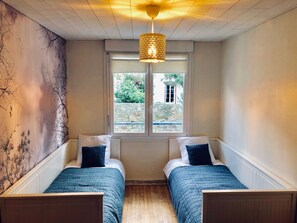 A room with two single beds, a large window with a view of greenery, and a textured wall. - Chez Alphonse: cosy, renovated T3 - near the port (VANNES)