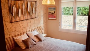 Une chambre avec un mur en pierre, un lit recouvert d’une courtepointe à rayures et une fenêtre donnant sur un paysage verdoyant.