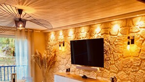 Une pièce avec un mur en pierre, un téléviseur fixé au mur et un ventilateur de plafond.
