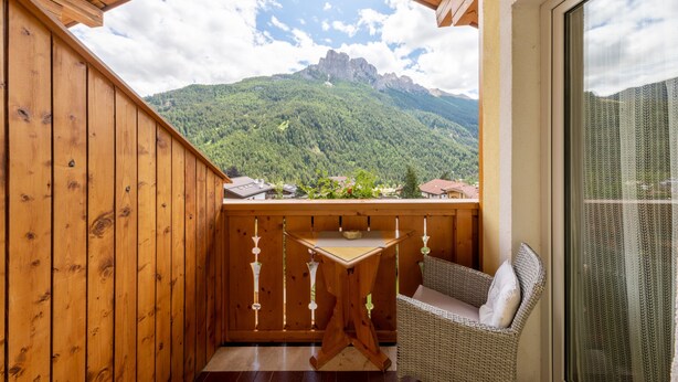 Een houten balkon met een tafel en stoel, met uitzicht op een bergachtig landschap.