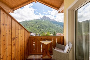A wooden balcony with a table and chair, overlooking a mountainous landscape. - Charming Apartment “Majon d’Aisciuda Vajolet” with Mountain View (Vigo di Fassa)
