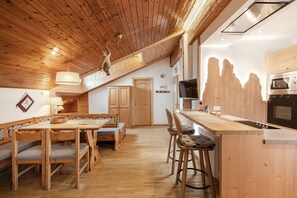 A wooden interior with a dining area, kitchen, and a loft space.