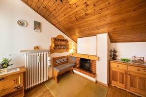 A cozy room with a wooden ceiling, a fireplace, a bench, and a wooden cabinet.