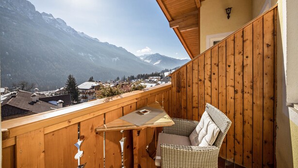 A balcony with a wooden railing, a wicker chair, and a table with a cushion.