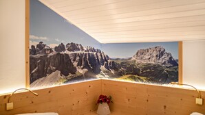 A room with a wooden ceiling, a large mountain landscape mural, and a small vase with red flowers on a wooden shelf.