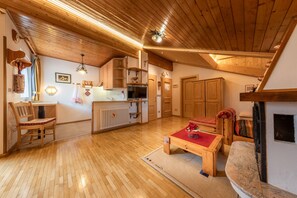 Un salón con suelo de madera, chimenea, una mesa de comedor y una cocina con armarios de madera.