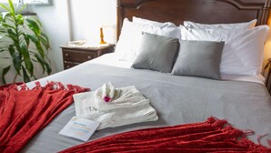 A neatly made bed with a red blanket, a white towel, and a card indicating bath towels are available. - Pool suite with marble bath in exotic fruit orchard (Ribeira Grande)