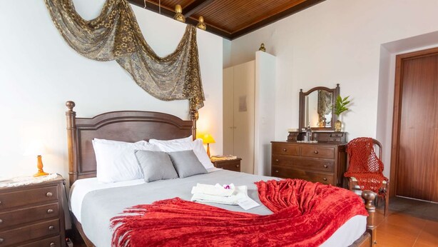 A bedroom with a wooden bed, a red throw blanket, a nightstand with a lamp, a dresser, and a mirror. - Pool suite with marble bath in exotic fruit orchard (Ribeira Grande)