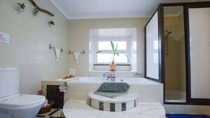 A bathroom with a toilet, sink, bathtub, and shower. There is a window with plants on the windowsill, a towel on the counter, and a blue mat on the floor. - Pool suite with marble bath in exotic fruit orchard (Ribeira Grande)
