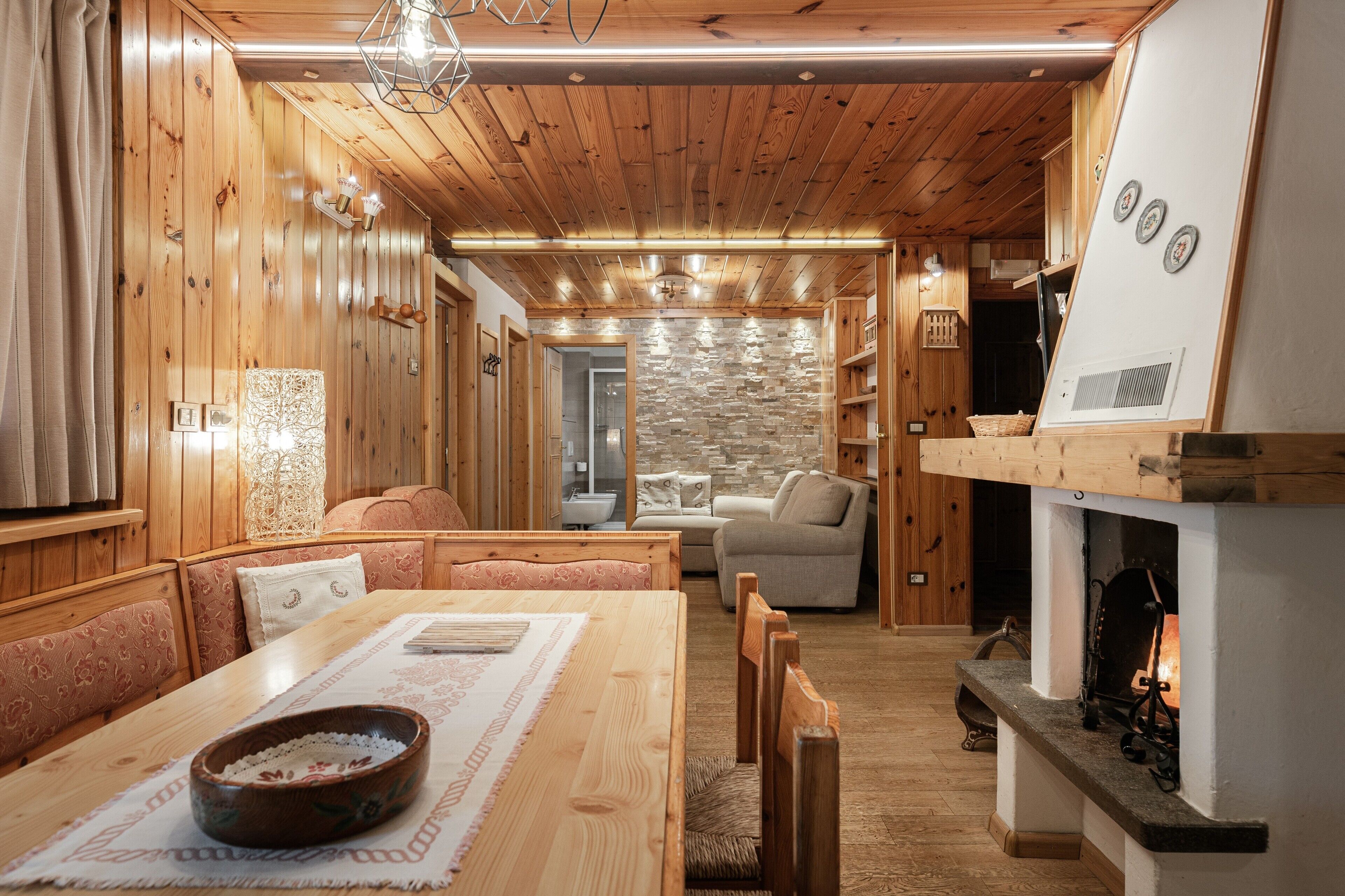 A cozy wooden interior with a dining area, seating, and a fireplace.