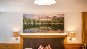 Une chambre à coucher avec un grand lit, une tête de lit, un tableau représentant un paysage de montagne accroché au mur, et deux lampes fixées au mur.