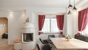 A modern kitchen with a built-in stove, a dining area with a wooden table and chairs, and a fireplace. - Charming Apartment “Majon d’Aisciuda Latemar” with Mountain View (Vigo di Fassa)