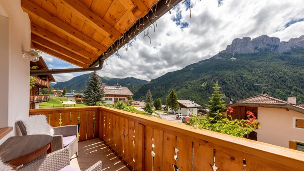 A wooden balcony with wicker furniture, overlooking a mountainous landscape. - Charming Apartment “Majon d’Aisciuda Latemar” with Mountain View (Vigo di Fassa)