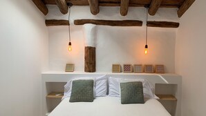 Une chambre avec un plafond en bois, un lit recouvert de linge de lit blanc, deux tables de chevet et une lucarne.