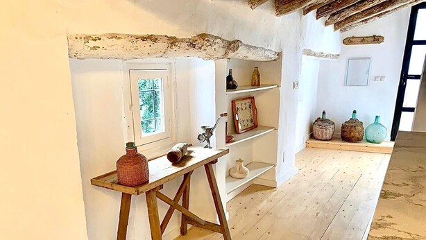 Une pièce avec un plancher en bois, une porte blanche, une fenêtre et une étagère contenant divers objets.
