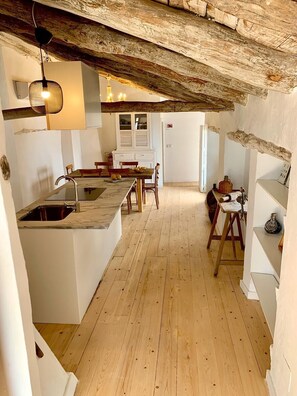 Una cocina compacta con suelo de madera, un lavabo, una mesa de comedor con sillas y una pequeña isla con una lámpara.