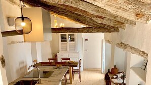 Een kleine keuken met een houten vloer, een spoelbak en een eethoek met stoelen en een tafel.