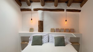 Een slaapkamer met een houten plafond, een bed met wit beddengoed, twee nachtkastjes en een plank met decoratieve objecten.