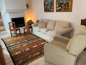 A living room with a sofa, chairs, a TV, a fireplace, and two paintings on the wall. - Holiday Home “Astarte House 6pax down” with Garden; Street Parking Available (Galera)