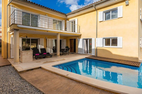 A two-story building with a swimming pool, outdoor seating, and a covered patio area.