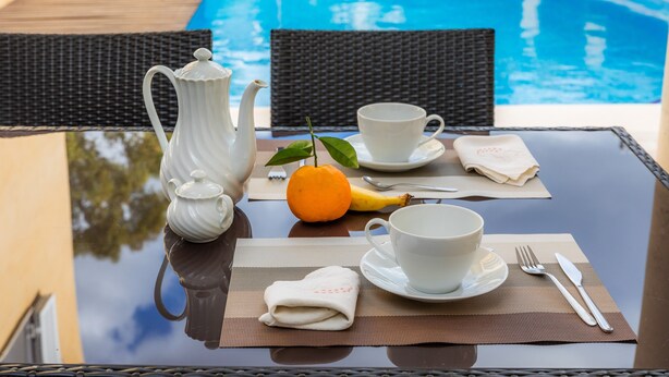 A table with a teapot, cups, a banana, and a napkin, near a poolside setting. - Holiday Home “Villa Can Gaya” with Pool, Terrace & Wi-Fi (Alcudia)
